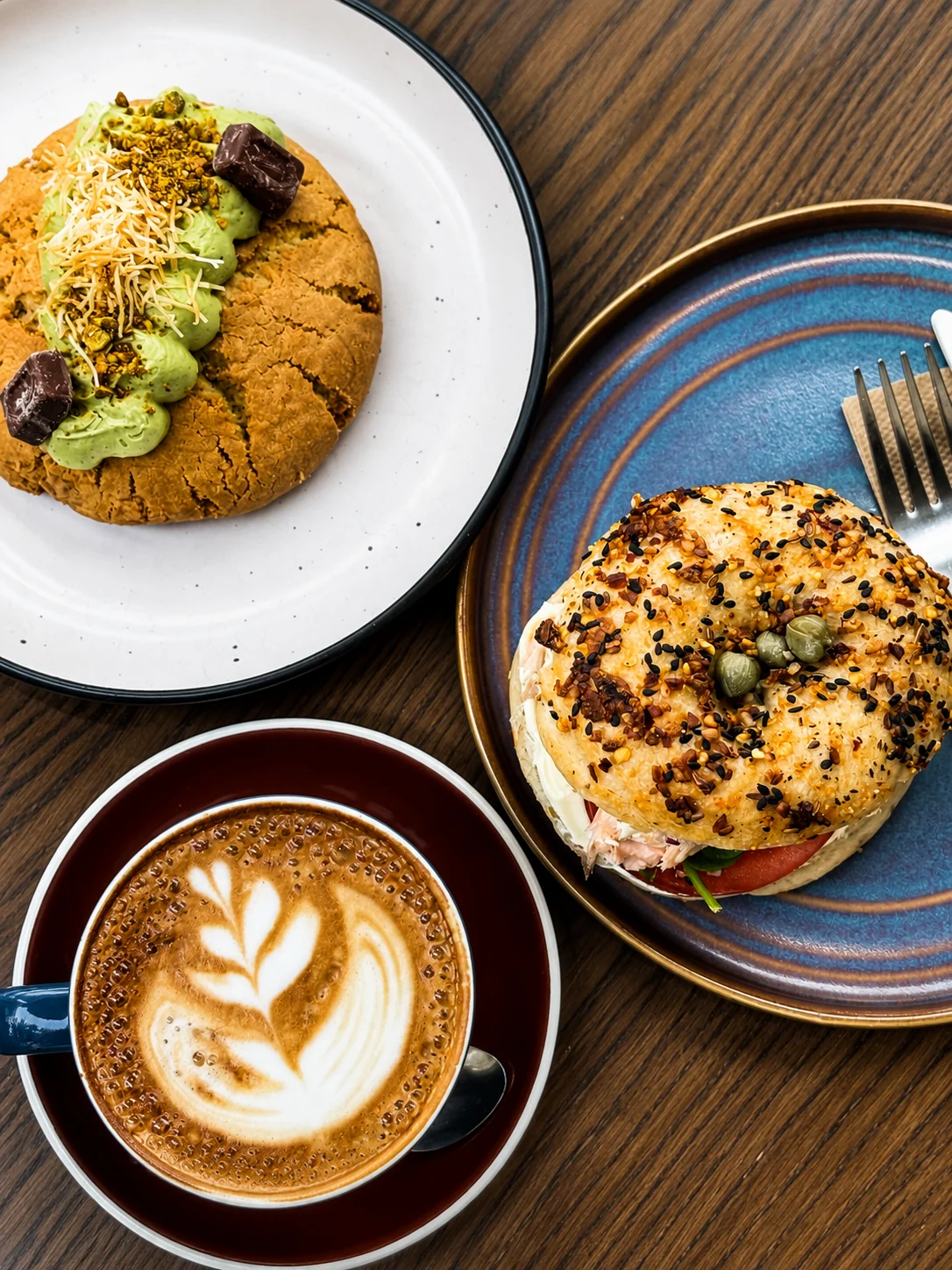 Latte, filled bagel and pistachio-topped biscuit on a table